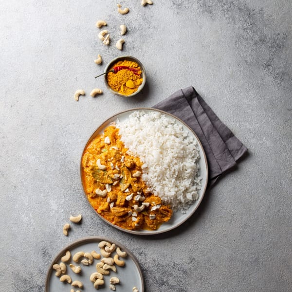 Indian chicken curry with rice, cashews, and a bowl of turmeric and chili on a gray surface.