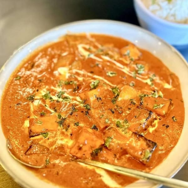 A close-up of a vibrant orange Indian curry dish with paneer, cream, and herbs.