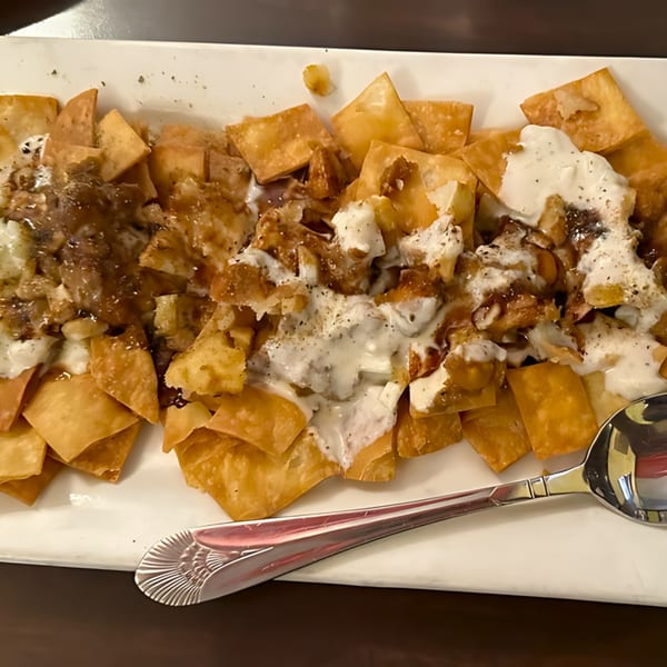 Crispy fried Indian flatbread pieces topped with yogurt, sweet chutney, and spices on a white plate.