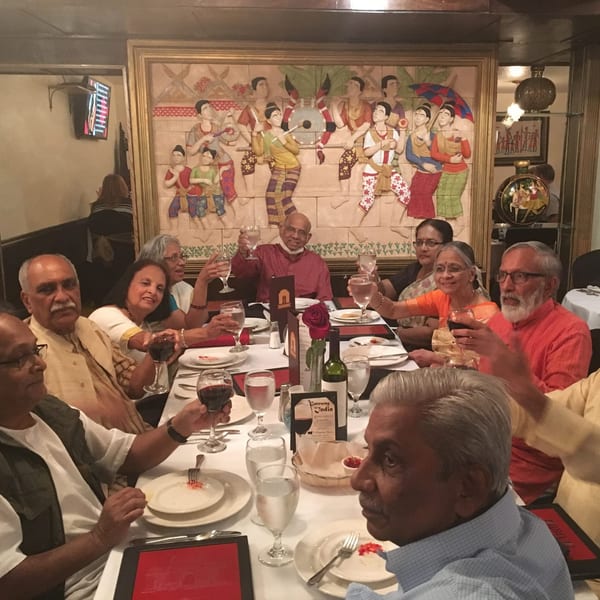 A group of people toasting with drinks at a long table in Gateway To India restaurant.