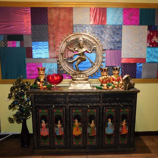 Indian decor featuring a golden Shiva statue, colorful fabric wall art, and painted wooden cabinet.