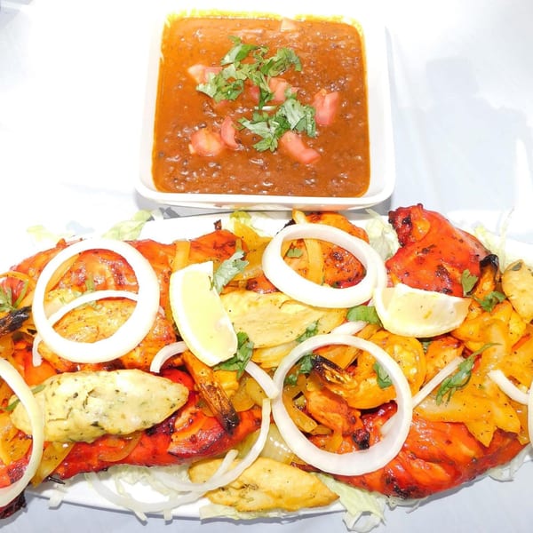 A platter of Indian tandoori chicken, shrimp, and fish with onion rings, lemon, and a side of dal.