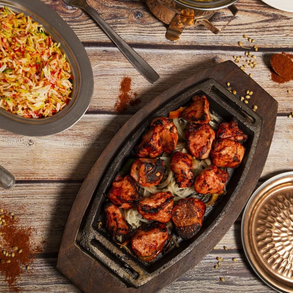 Overhead view of grilled Indian chicken tikka with onions, colorful rice, and spices on a wooden table.