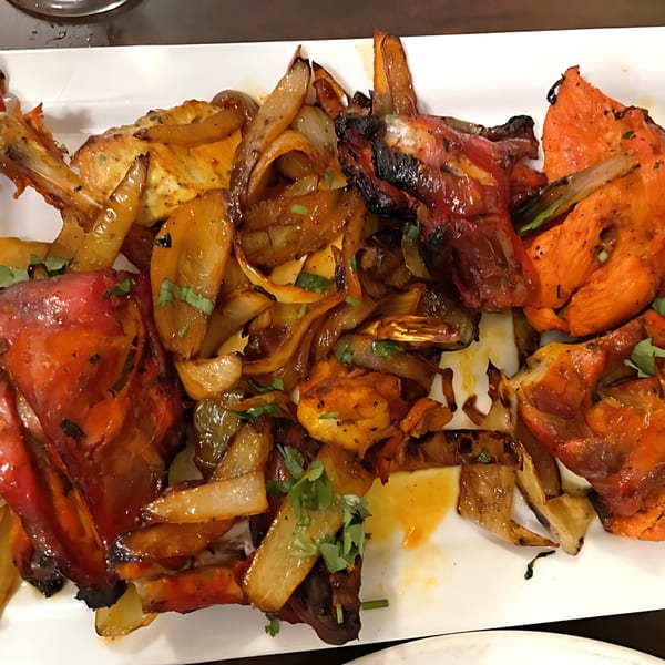 A white platter filled with vibrant orange Tandoori chicken and sautéed onions, garnished with fresh herbs.
