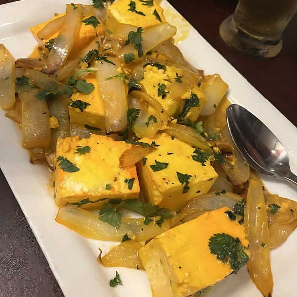 Indian paneer dish with yellow cheese cubes, sautéed onions, and fresh cilantro on a white plate.