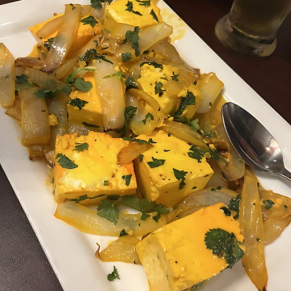 Indian paneer dish with yellow cheese cubes, sautéed onions, and fresh cilantro on a white plate.